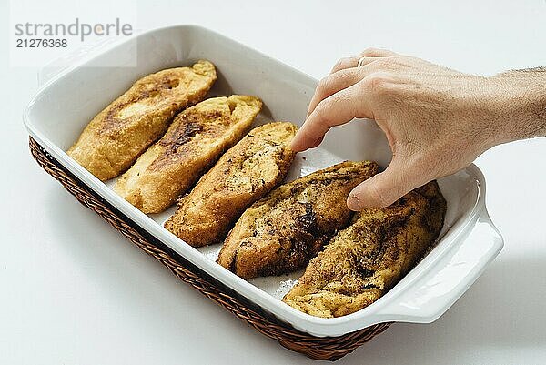 Männliche Hand  die torrijas  ein typisch spanischer süßer gebratener Toast aus in Eiern und Milch getränktem Brot auf einem Tablett nimmt  vor weißem Hintergrund. Traditionelle Nachspeise für Fastenzeit und Ostern