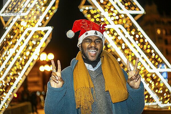 Porträt eines coolen afrikanischen jungen Mannes  der erfolgreich eine Weihnachtsmannmütze trägt  nachts in der Stadt zu Weihnachten