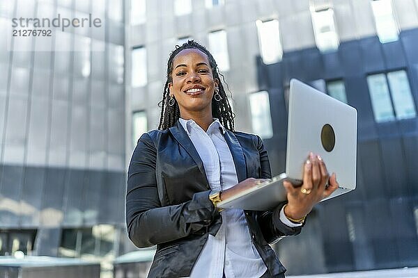 Porträt einer lässigen lateinischen Geschäftsfrau  die mit einem Laptop im Freien im Finanzviertel steht