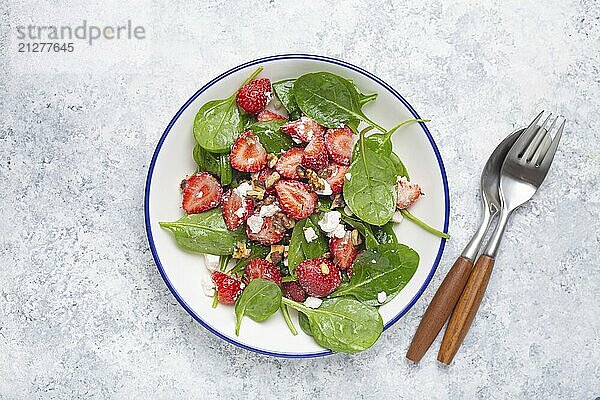 Leichter gesunder Sommersalat mit frischen Erdbeeren  Spinat  Frischkäse und Walnüssen auf weißem Keramikteller  weißer rustikaler Stein Hintergrund von oben  Foodfotografie