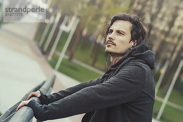 Porträt eines jungen Mannes  der auf der Brücke steht und Musik hört und die schöne Aussicht genießt