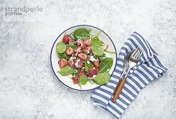 Leichter gesunder Sommersalat mit frischen Erdbeeren  Spinat  Frischkäse und Walnüssen auf weißem Keramikteller  weißer rustikaler Stein Hintergrund von oben  Foodfotografie  food photography  food photography