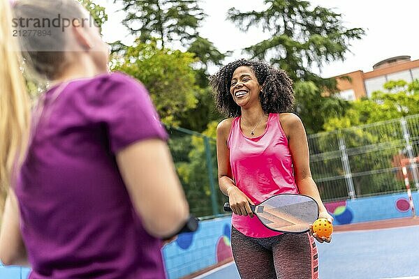 Fröhliches Paar multiethnischer Frauen spielt Pickelball auf einem Platz im Freien