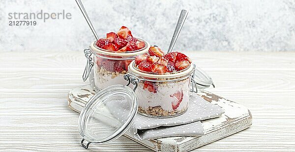 Parfait mit frischen Erdbeeren  Joghurt und knusprigem Müsli in durchsichtigen Einmachgläsern auf weißem  rustikalem Holzhintergrund aus der Vogelperspektive  gesundes Frühstück oder leichtes Sommerfruchtdessert  Foodfotografie  food photography  food photography