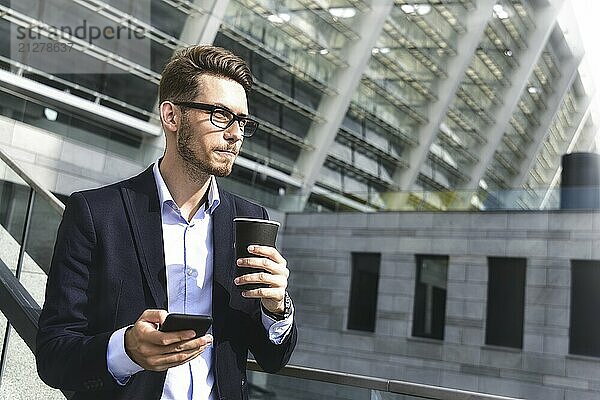 Gutaussehender erfolgreicher Geschäftsmann in elegantem Anzug steht draußen auf der Straße in der Stadt mit Kaffee