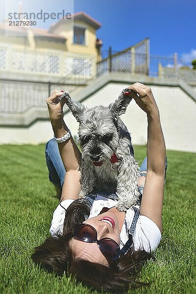 Hübsche erwachsene kaukasische glückliche Frau ruht im Park an einem sonnigen Tag mit ihrem geliebten Hund. Weibliche lag auf dem Gras lächelnd und Blick in die Kamera