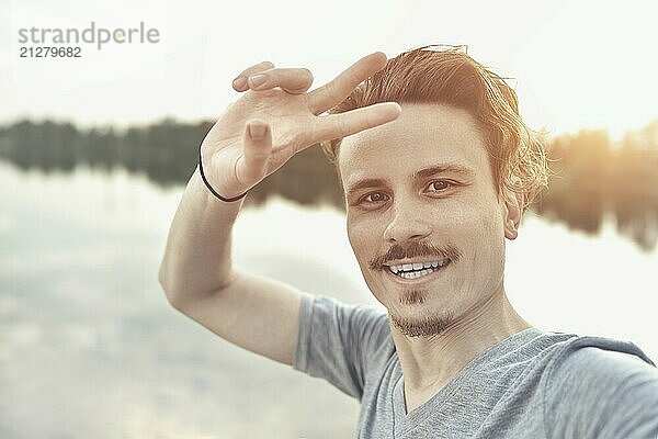 Porträt des jungen gut aussehend stilvoll lächelnd Kerl macht selfie gegen den See. schöne Natur