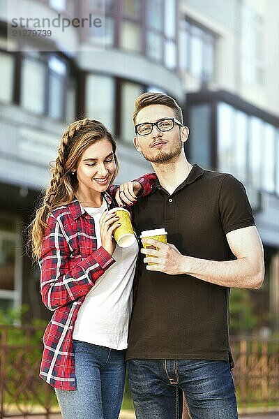 Porträt eines glücklichen Paares  das mit Kaffee auf der Straße spazieren geht