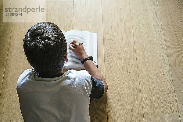 Kleiner Junge  der ein Buch liest. Er liegt auf dem Boden. Rückansicht  selektiver Fokus