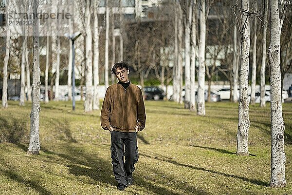 Modischer junger schwuler Mann mit brauner Jacke  der in einem Park in die Kamera schaut