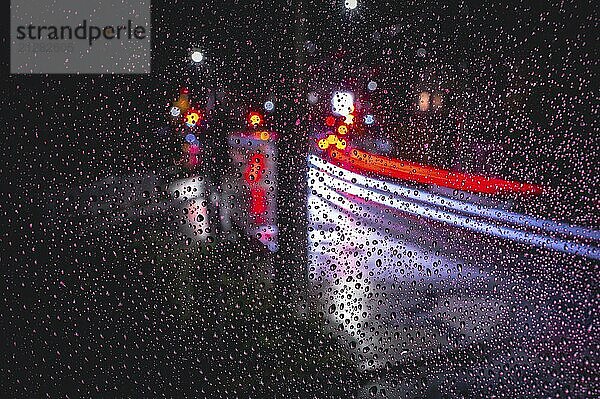 Regen fällt auf eine Glasscheibe  unscharfe Lichtspuren von Fahrzeugen und Straßenlaternen in der Nacht erzeugen ein Bokeh-Effekt  Jena  Thüringen  Deutschland  Europa