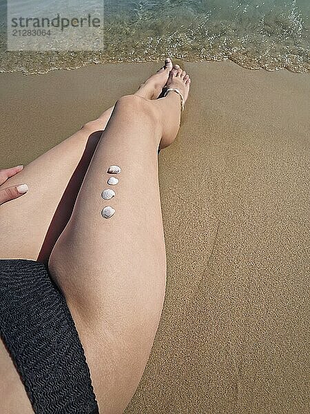 Closeup schöne junge Frau Beine mit kleinen Muscheln auf der weichen Haut  Gerben am Strand durch das Wasser. Seaside Entspannung und Urlaub genießen Konzept