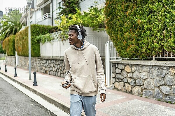 Junger afrikanischer Mann  der Musik hört und die Straße in einem Wohngebiet entlanggeht