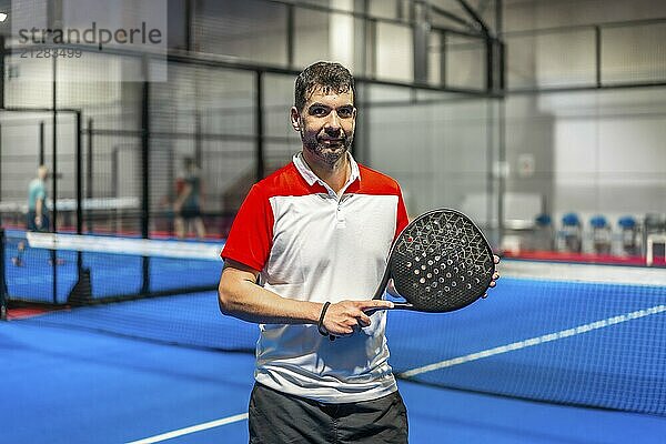 Porträt eines sportlichen reifen Mannes mit Paddle Tennisschläger auf einem blauen Indoor Paddle Platz