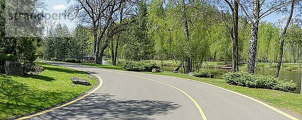 Straße durch den Park. Asphaltierter Weg für Fußgänger und Radfahrer durch schöne Grünanlagen und einen See im Park