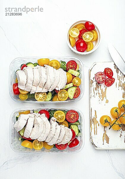 Gesunde Mahlzeit Vorbereitung für das Mittagessen  Diät gekochtes Hühnerfilet mit Gemüse Salat in Lunch Boxen Container Draufsicht auf weißen Marmor Küchentisch Hintergrund mit Messer und Schneidebrett  Lebensmittel Fotografie