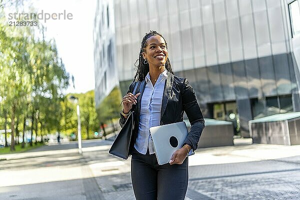 Selbstbewusste lateinamerikanische Geschäftsfrau  die das Büro verlässt und ihren Laptop durch die Stadt trägt