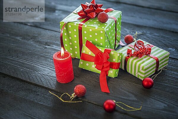 Fröhliches Bild mit einem Bündel grün eingepackter Geschenke  gebunden mit roten Bändern und Schleifen  umgeben von Weihnachtsschmuck und einer brennenden Kerze  auf einem Holztisch