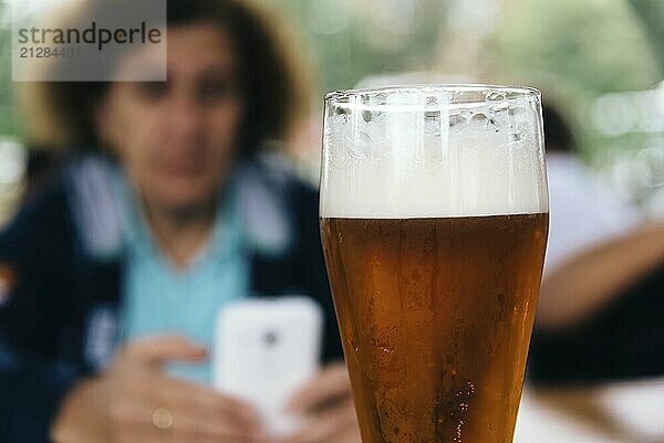 Nahaufnahme eines erfrischenden Pint Lagerbieres gegen eine Frau  die eine SMS auf ihrem Smartphone schreibt. Selektiver Fokus