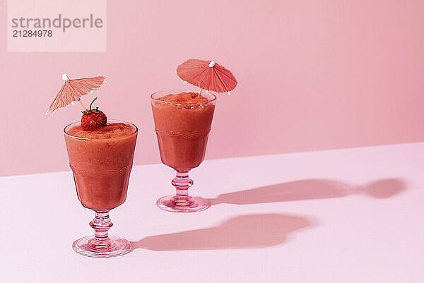 Zwei Erdbeer Smoothie in einem Glas mit Cocktail Regenschirm auf einem rosa Hintergrund  in grellem Licht. Sommer leckere Mocktails. Gesundes diätetisches Getränk