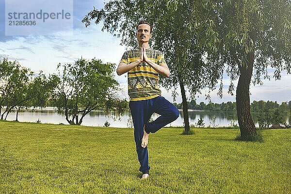 Fitness Mann macht Übung auf einem Bein isoliert im Park. Genießen Sie die Natur  Yoga und Meditation Konzept. spirituellen Praktiken