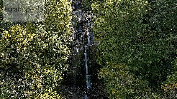 Ein wunderschöner Wasserfall in einer Berglandschaft  während sich die Blätter im Herbst verfärben