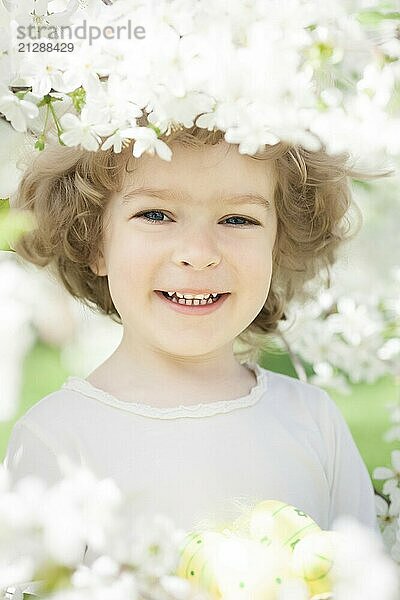 Glückliches Kind hält Ostereier vor einem Hintergrund mit Frühlingsblumen