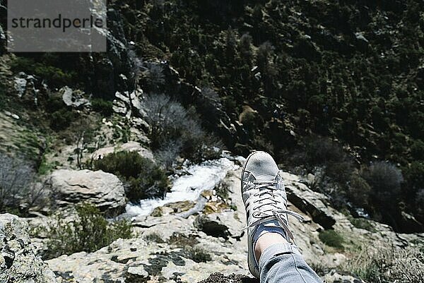 Mann in Turnschuhen aus persönlicher Sicht bei der Betrachtung eines schönen Wasserfalls in einer Berglandschaft im Madrider Gebirge. Fokus auf den Vordergrund