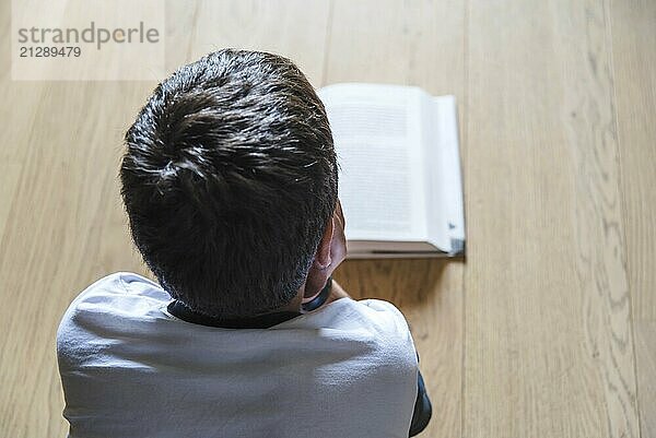 Kleiner Junge  der ein Buch liest. Er liegt auf dem Boden. Rückansicht  selektiver Fokus