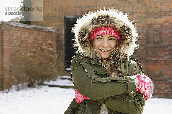 Smiling Teenage Girl Wearing Parka Hugging Herself Outdoors