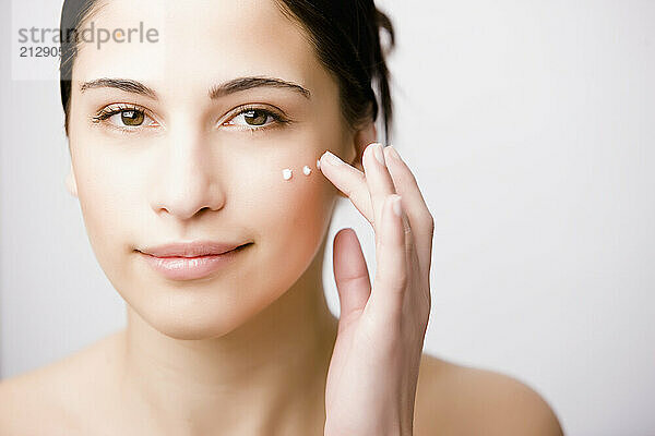 Close up of a young woman applying moisturizer on her cheek