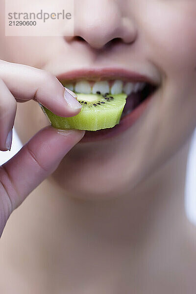 Extreme close up of a woman biting a kiwi slice