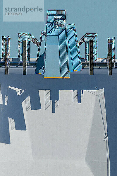 View from above diving platforms and diving boards casting shadows above sunny  empty swimming pool