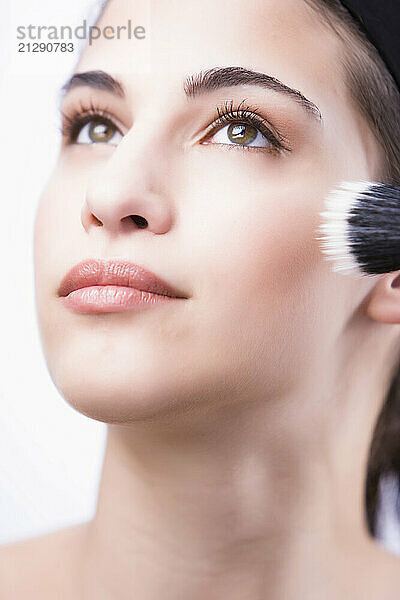 Close up of a young woman applying make with a blush brush