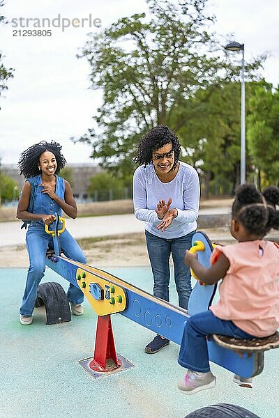 African young moother and grandmother encouraging a little girl in the playground