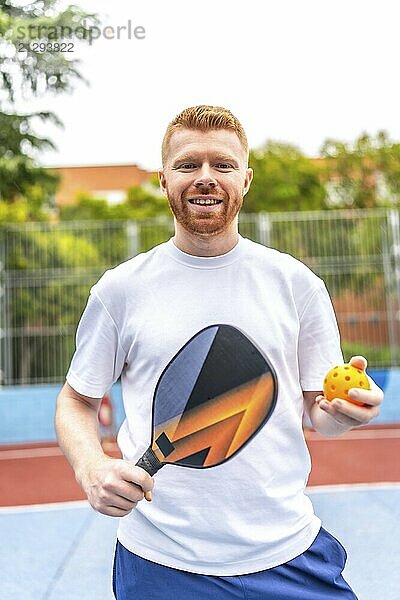 Vertical portrait of a male caucasian and sportive pickelball player in an outdoor court