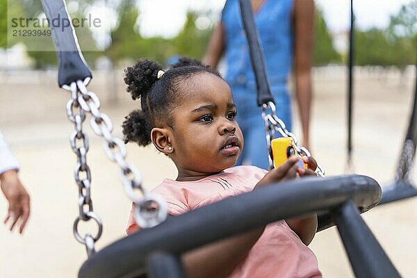 An african little schoolgirl swinging in the park next to her family