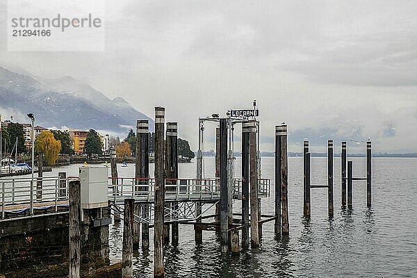 Amazing foggy view on pier and town Locarno in distance and autumn leaf color nature and Swiss Alps  snowcapped mountains -Swiss Alps