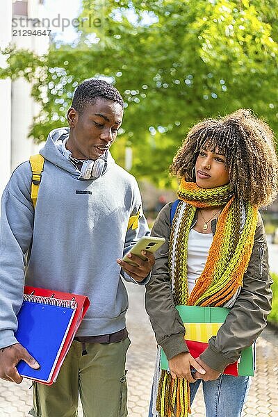 Vertical photo of two multi-ethnic latin and african students using mobile phone while walking along the university campus