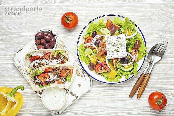 Traditional Greek Food: Greek Salad  Gyros with meat and vegetables  Tzatziki sauce  Olives on White rustic wooden table background top view. Cuisine of Greece  food photography  food photography