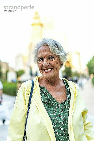 Vertical close-up portrait of a happy elder modern woman standing in the city smiling at camera