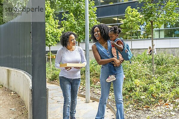 African mother carrying a girl in arms while walking with grandmother along a park