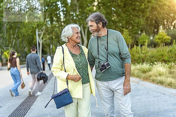 Three quarter length photo of a caucasian cute senior couple walking together along a city park