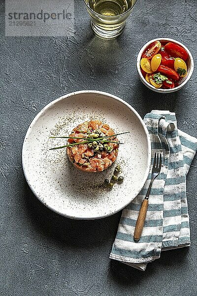 Food  SALMON TARTAR with capers and purple onion on white plate  gray background