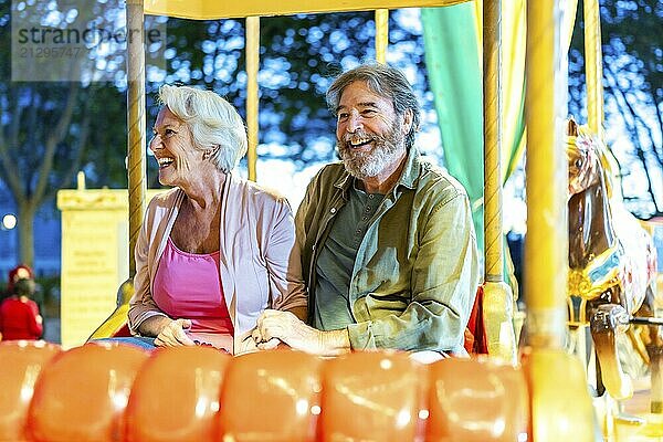 Happy caucasian senior couple enjoying a ride with carousel at night in the city