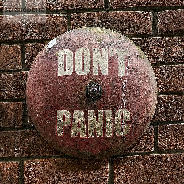 Isolated Rustic Vintage Red Alarm Bell With The Words Don't Panic In White Against A Red Brick Wall