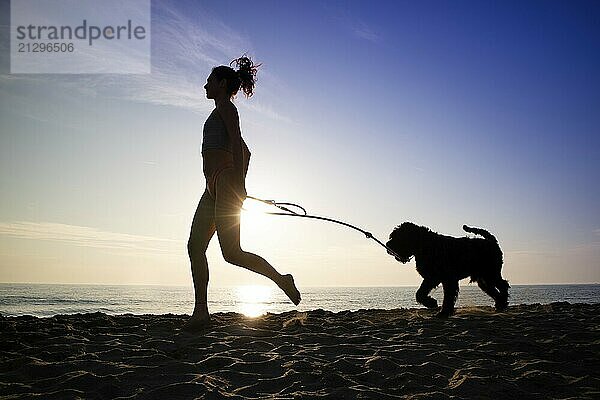 Girl running in the company of her dog on the seashore shot against the light