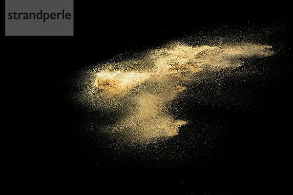 Golden sand explosion isolated on black background. Abstract sand cloud. Golden colored sand splash against dark background. Yellow sand fly wave in the air