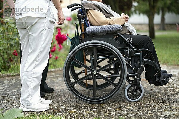 Senior woman in wheel chair with relative and nurse caregiver  outdoors at nursing home garden. graphy