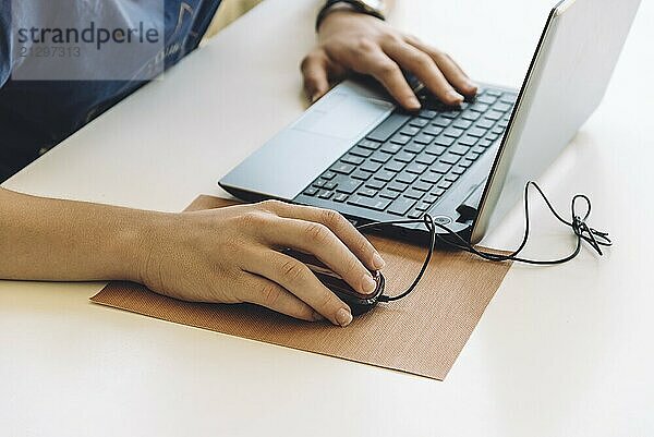 Young man working with laptop  hands on notebook computer and mouse. Blurred background. Student working at home